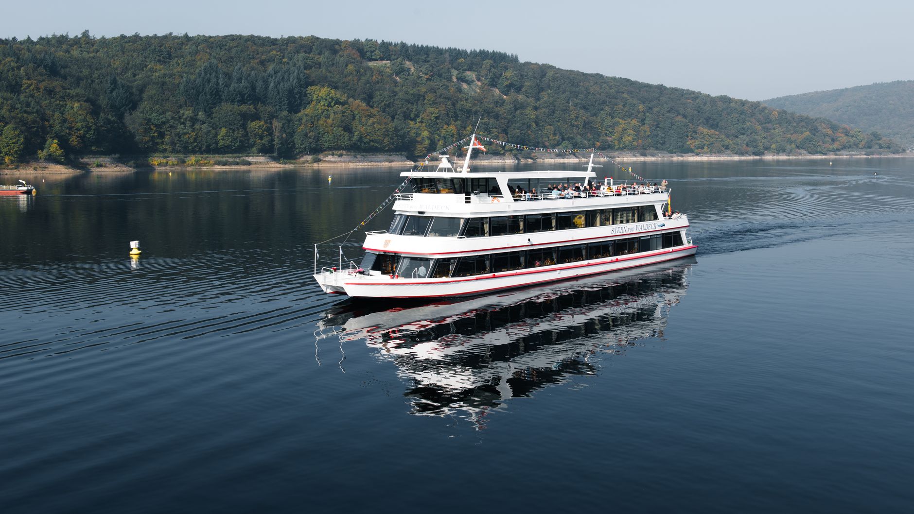 Ferry cruising on Edersee Reservoir with a serene forest backdrop in Hessen, Germany.